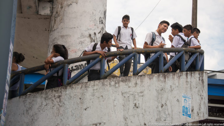 Uniformed students with backpacks gathered along a concrete stairway with blue metal railings.