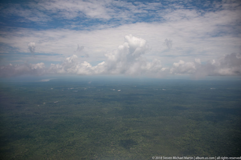 Aerial view across an extensive green Amazon forest beneath large storm clouds.