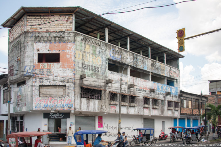 Weathered multi-story building with faded wall advertisements, open upper bays, and mototaxis along the street.