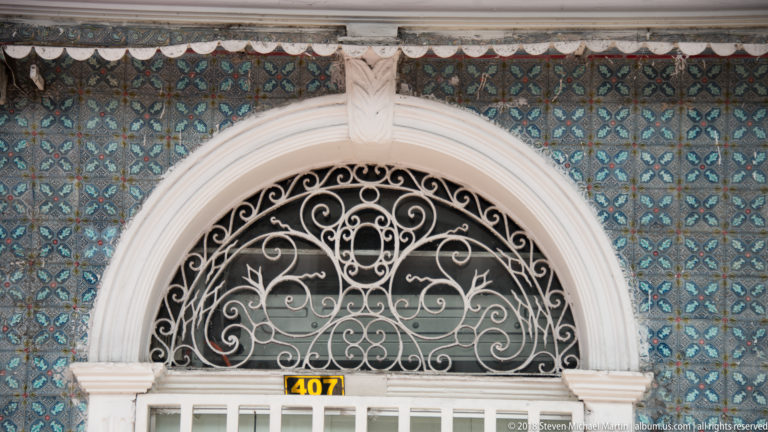 Arched doorway at number 407 with white molding, scrolling iron transom, and blue patterned tile wall.