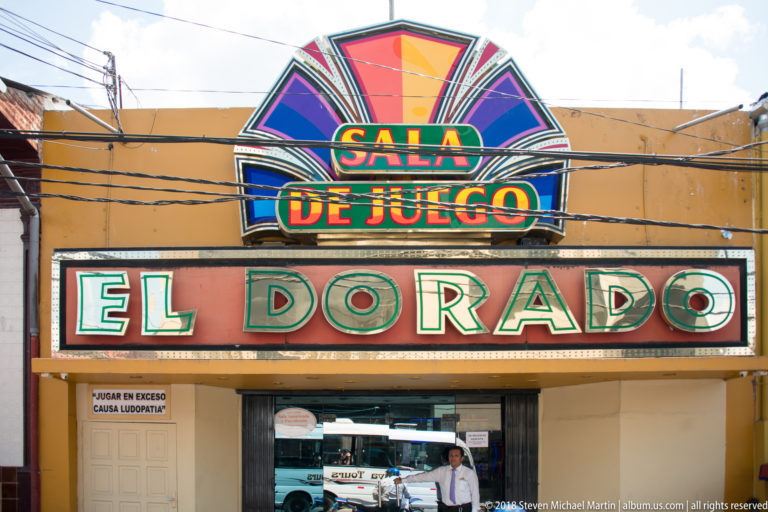 Entrance to Sala de Juego El Dorado beneath a large multicolored sign and overhead utility wires.