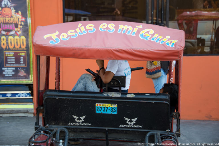 Red-canopied mototaxi at a curb with “Jesús es mi Guía” painted across the roof.