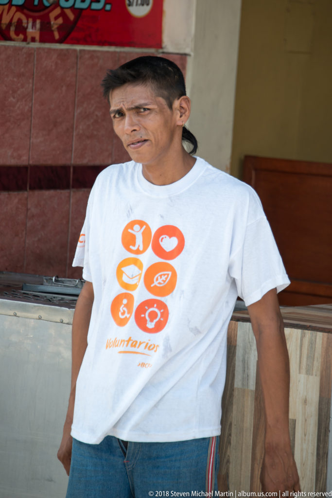 Man in a white T-shirt standing beside a storefront counter on an Iquitos street.