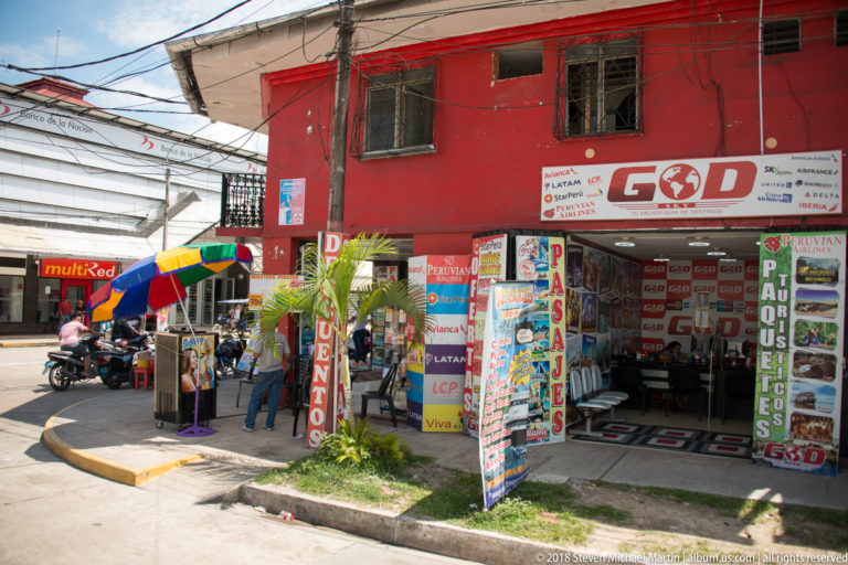 Red Iquitos travel-service storefront covered with tour and passage signs beside a busy corner sidewalk.