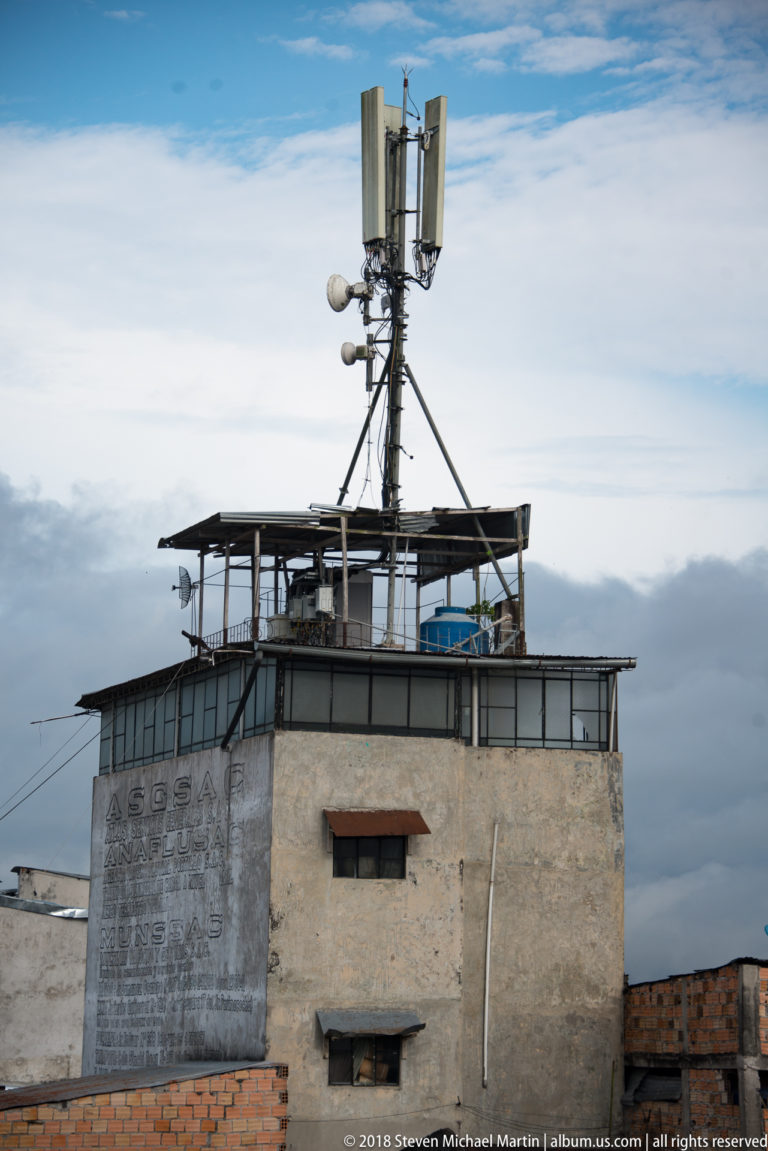 Panel antennas and communications equipment mounted on a rooftop mast against a cloudy Iquitos sky.