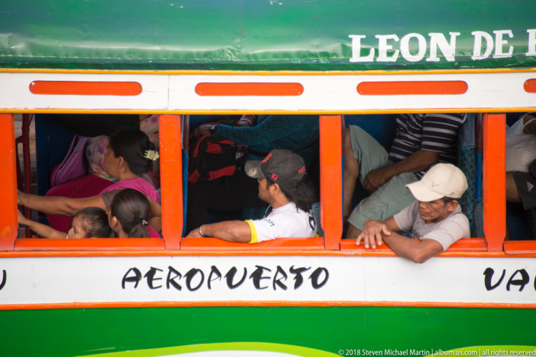 Crowded passengers lean beside open windows of a green-and-white Iquitos bus marked Aeropuerto.