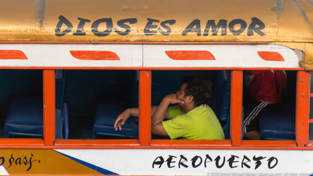Passenger in a green shirt seated beside an open orange-framed bus window marked Aeropuerto.
