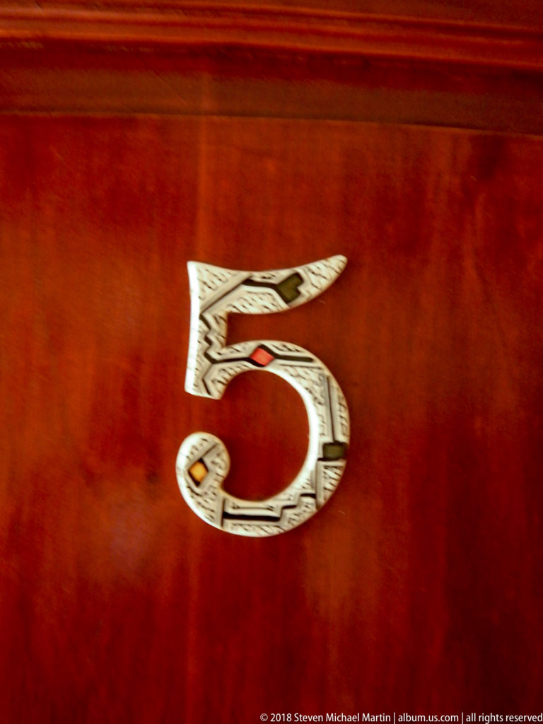 Ornamented pale number 5 inlaid into a polished reddish wooden surface.