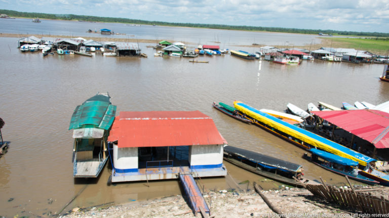 Elevated view of floating dock buildings and long colorful passenger boats along the muddy Iquitos riverfront.
