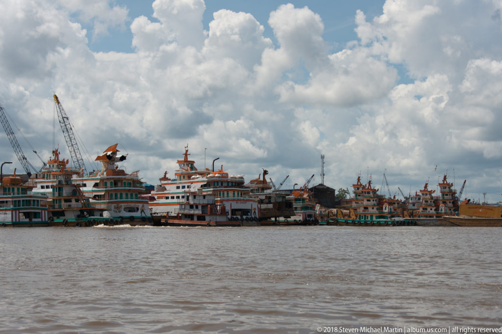 Wide river view of many moored boats and work vessels at Iquitos, with cranes rising behind the waterfront.