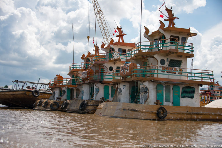 Decorated river workboat with turquoise railings, tiered roof ornaments, and tire fenders along its brown hull.