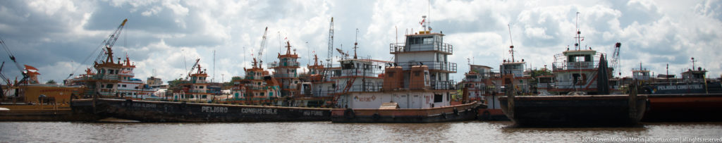 Cluster of weathered tugboats and work vessels with tall wheelhouses moored closely together at the Iquitos riverfront.