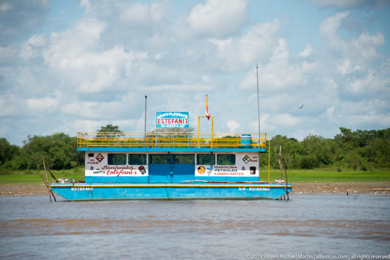 Blue and yellow river ferry named Estefani seen broadside against a low green riverbank.