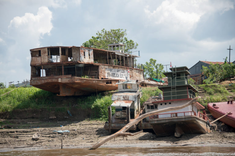 Weathered wooden riverboats and hulls hauled onto a muddy bank at a working waterfront near Iquitos.