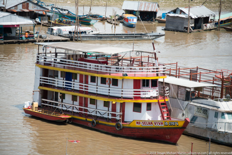 Multi-deck riverboat M/F Selva Viva II with red railings, white cabins, yellow trim, and tire fenders.