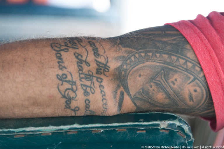 Close view of a tattooed forearm with script and circular portrait motif resting on a worn green boat seat.