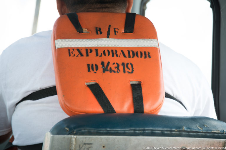 Orange life jacket stenciled 'EXPLORADOR II 4319' hanging against a worn seat back inside a river boat.