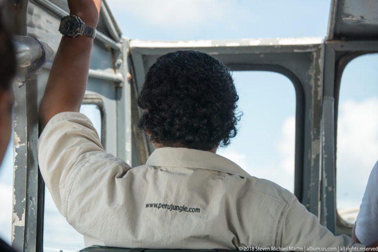 Back view of a boat crew member in a light shirt looking forward through the open frame of a river launch.