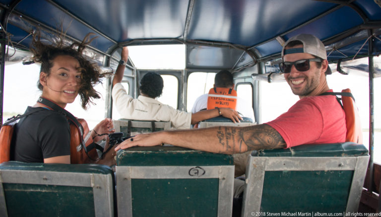 Passengers look back from bench seats while two crew members face forward inside a small covered river launch.