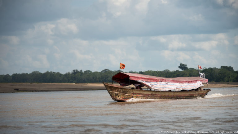 Small wooden riverboat with red-and-white canopy traveling across open water near Iquitos.