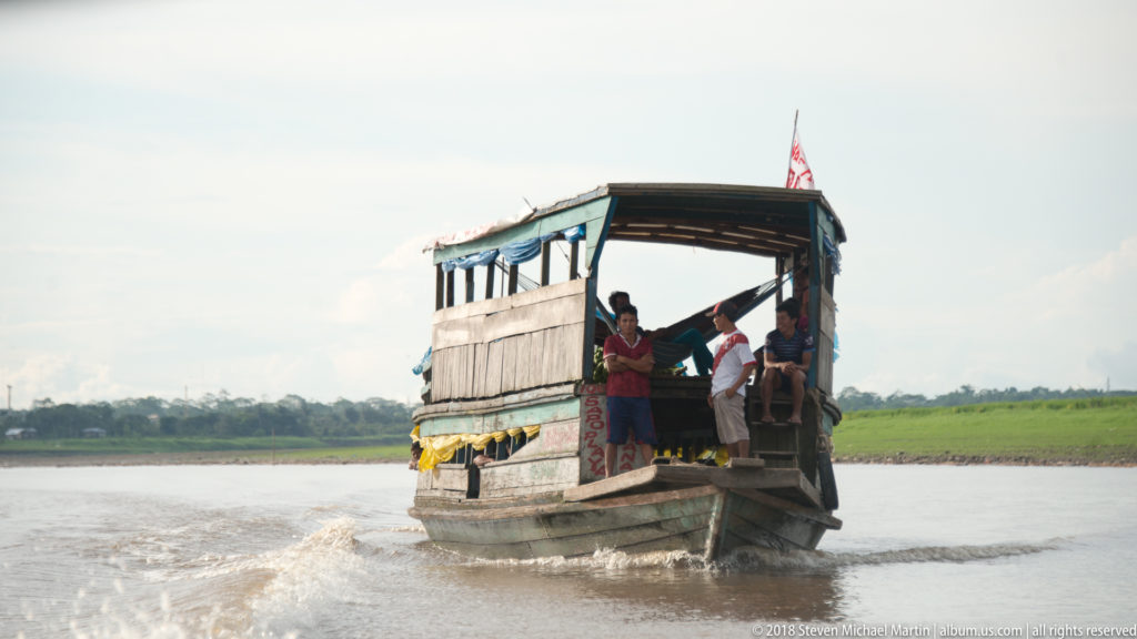 Covered wooden river launch approaching with several passengers standing at the open stern.