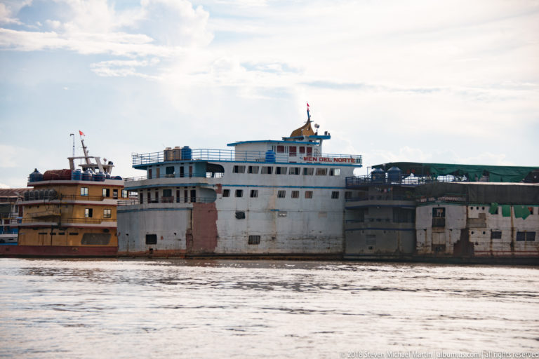 Large white multi-deck river vessel moored beside another boat at the Iquitos waterfront.