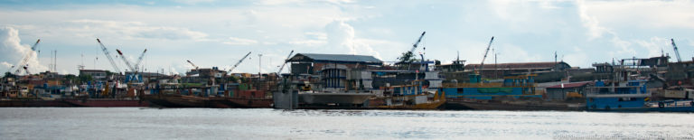 Crowded line of working riverboats with overlapping wheelhouses, masts, and painted hulls at Iquitos.