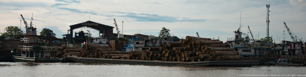 River cargo boat heavily loaded with rough-cut logs along the Iquitos waterfront.