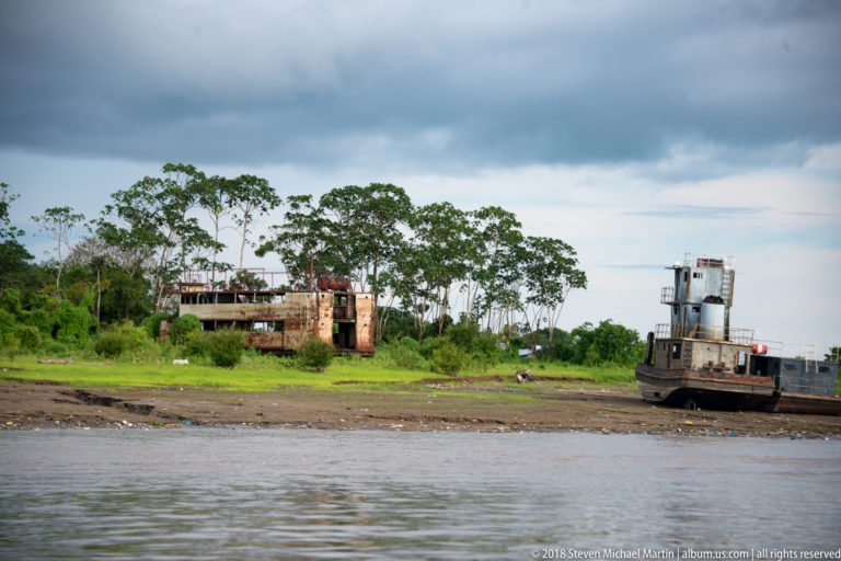 Grounded workboats and a rusting vessel hulk spread along a low tropical riverbank near Iquitos.