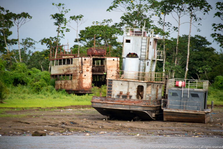 Weathered workboat grounded on an exposed bank beside a rusting, partly dismantled vessel.