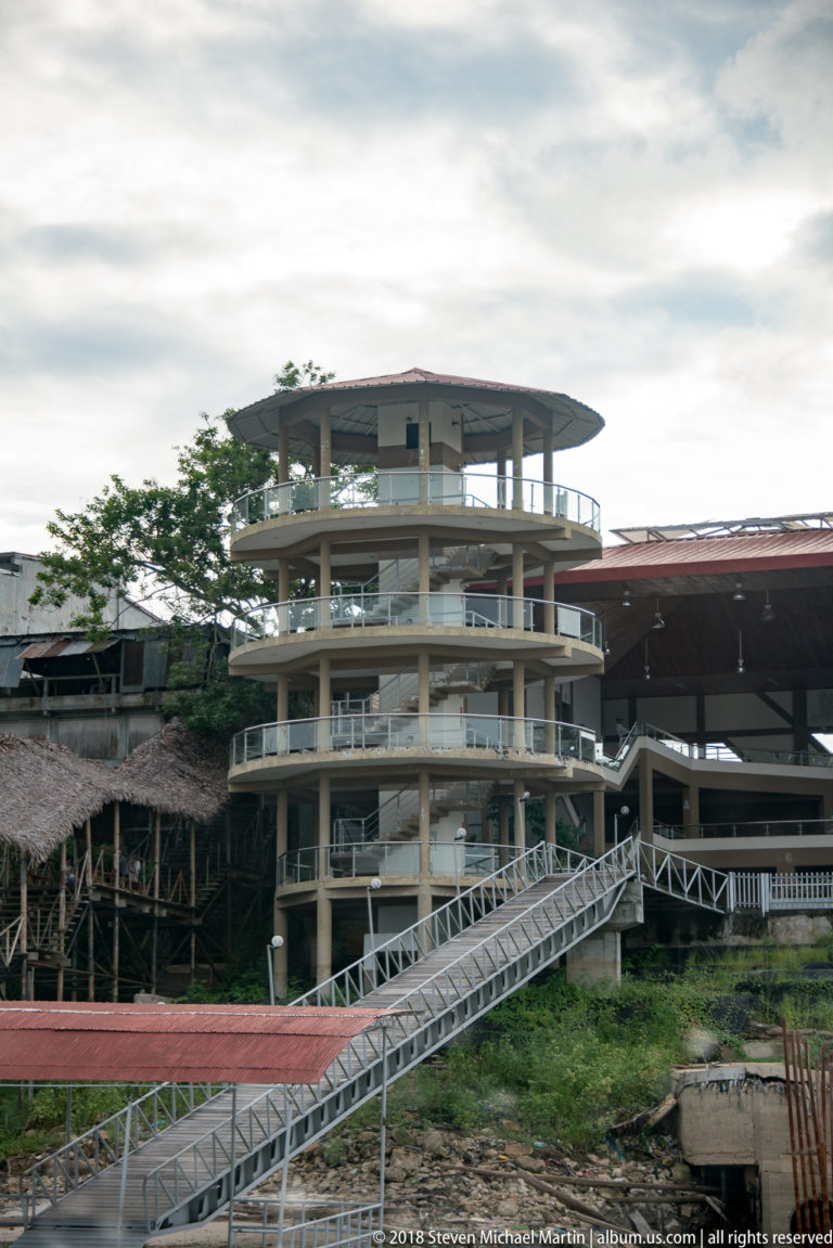 Multi-level concrete waterfront building connected by elevated metal gangways near the Iquitos docks.