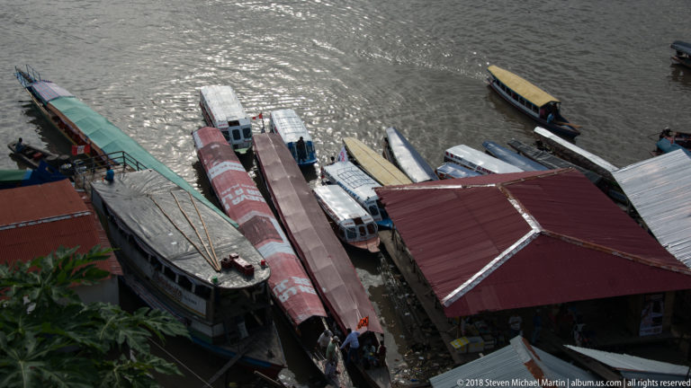 Passenger boats packed closely beside roofed dock structures and gangways at the Iquitos waterfront.