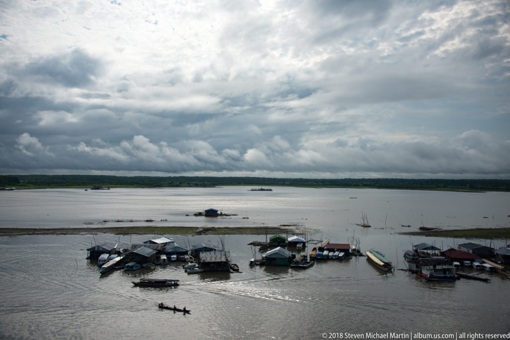 Small boats and floating dock structures beneath dark storm clouds on the river at Iquitos.