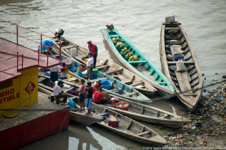 People transfer produce and supplies among narrow wooden boats at a riverside landing in Iquitos.