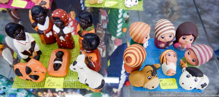 Overhead display of colorful human and animal figurines on woven mats with handwritten 25.00 and 35.00 price tags.