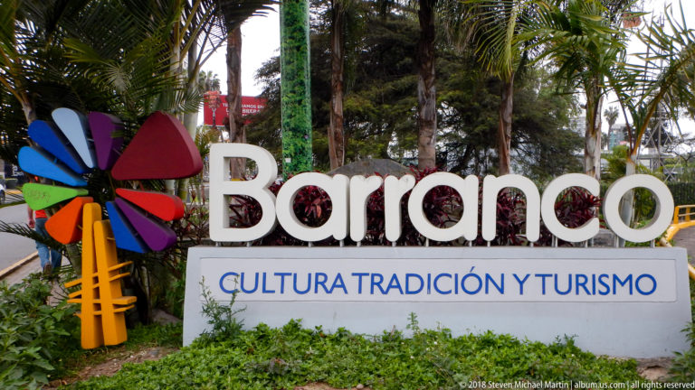 White Barranco sign with colorful emblem and the words Cultura Tradición y Turismo among palms and greenery.