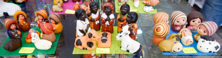 Colorful small human and animal figurines arranged on woven mats with handwritten price tags in a shop display.