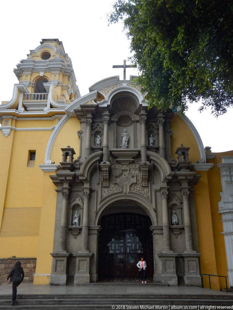 Full gray ornamental church portal against yellow walls, with people standing near the dark entrance.
