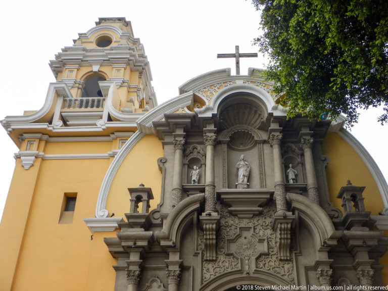 Upper church portal with twisted columns, sculptural niches, layered moldings, curved yellow façade, and cross.