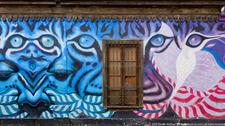 Blue, violet, black, and pink animal mural surrounding a traditional wooden window with iron grille.