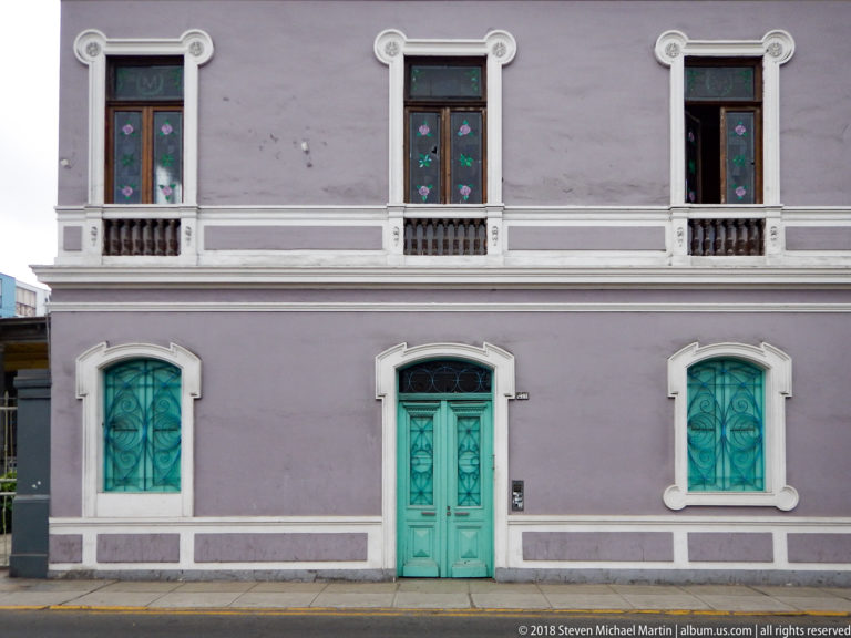 Lavender two-story façade with turquoise central door and windows, white trim, and small upper balconies.