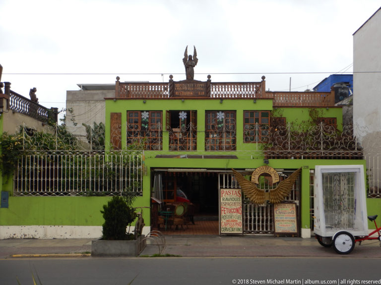 Bright green restaurant façade with open entrance, menu board, decorative metal fence, colored windows, and rooftop ornament.