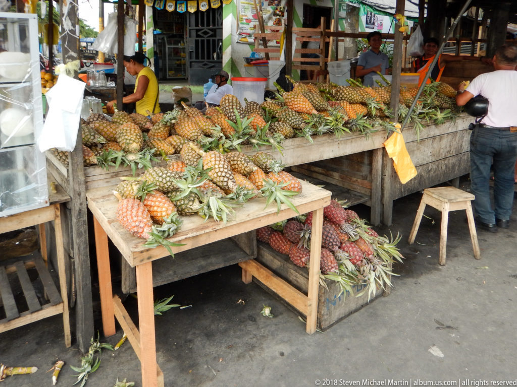 Dozens of pineapples cover rough wooden tables at a busy fruit stall in Iquitos Market.