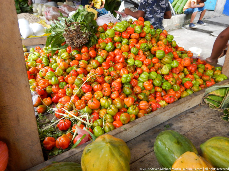 Large mound of red and green peppers fills a market table, with papayas along the front edge.