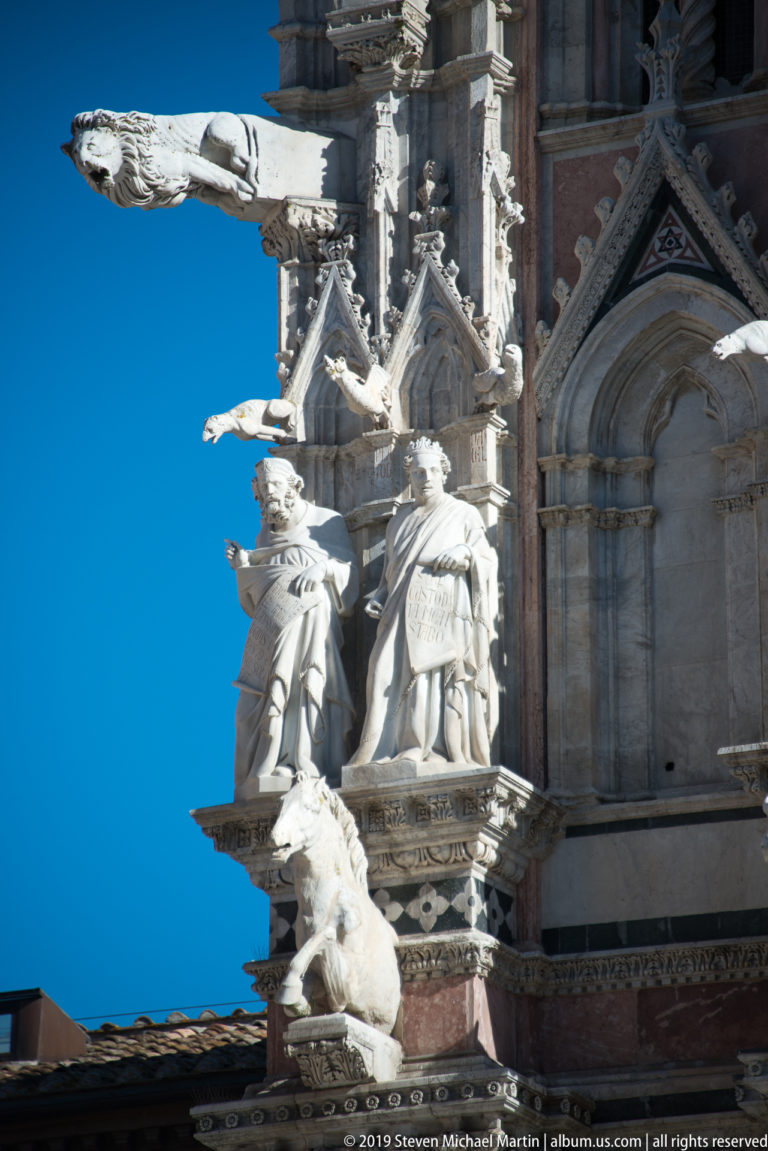 Pale statues stand among pointed gables, finials, and carved marble bands.