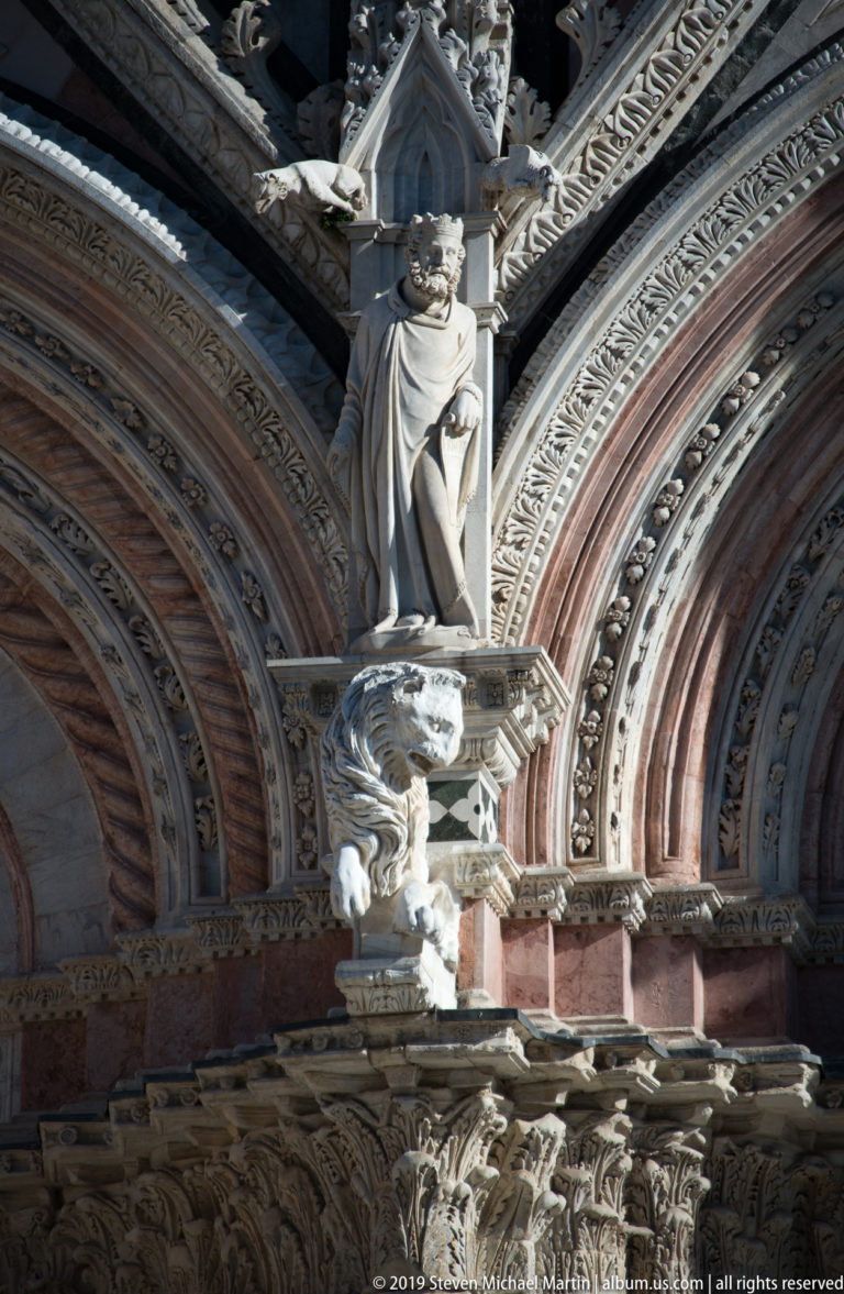 A robed statue stands above a projecting animal-like carving on the cathedral façade.