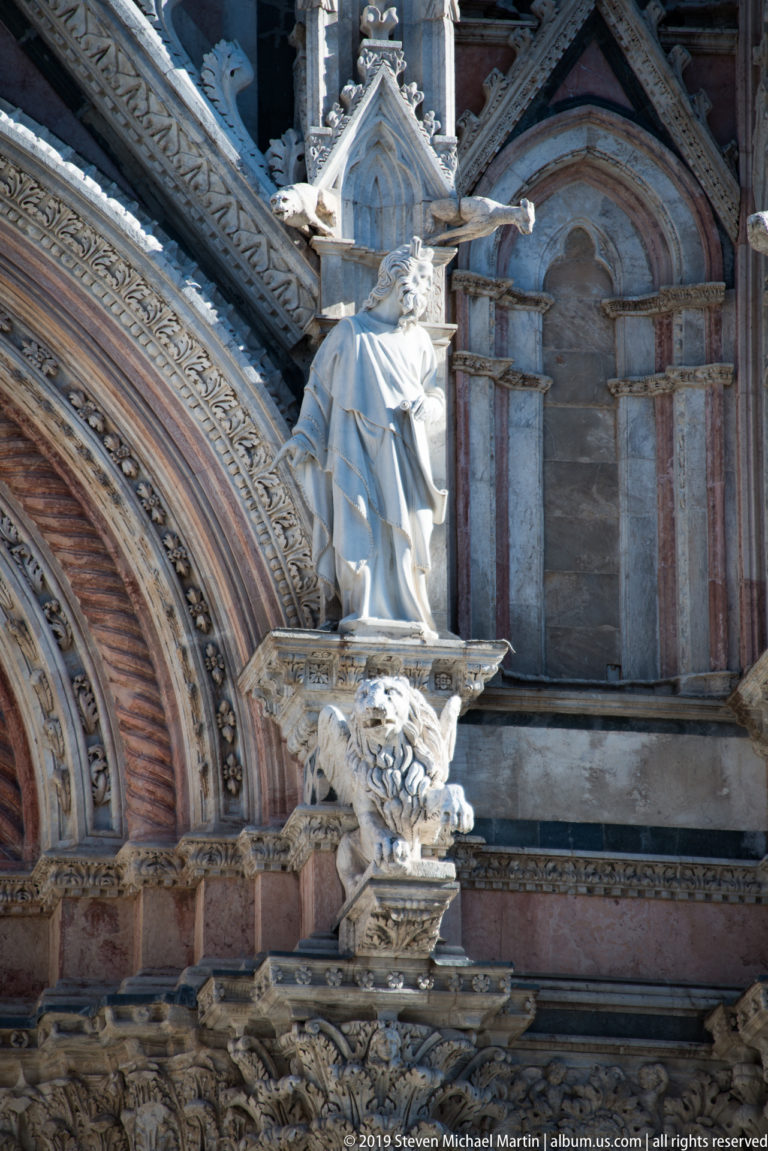 A seated robed figure holding a cross occupies a carved niche in the cathedral façade.