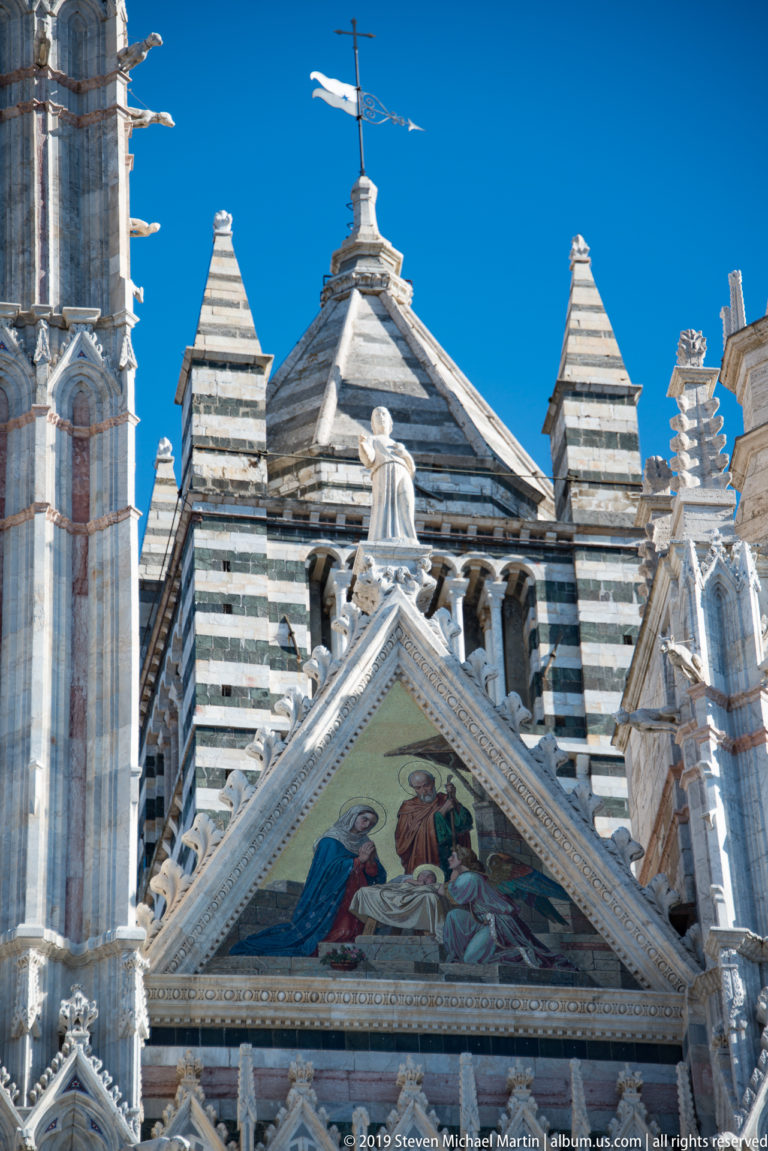 A figurative mosaic fills the cathedral’s triangular gable below a winged statue.