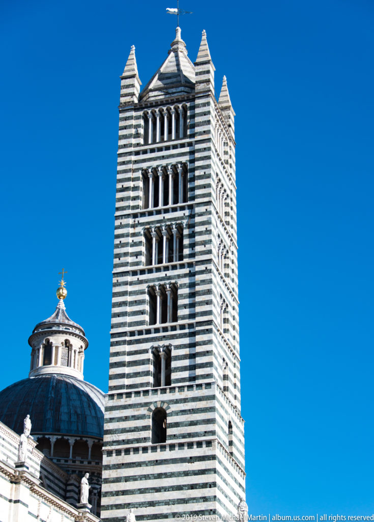 The striped campanile rises beside the cathedral’s dark dome and small lantern.