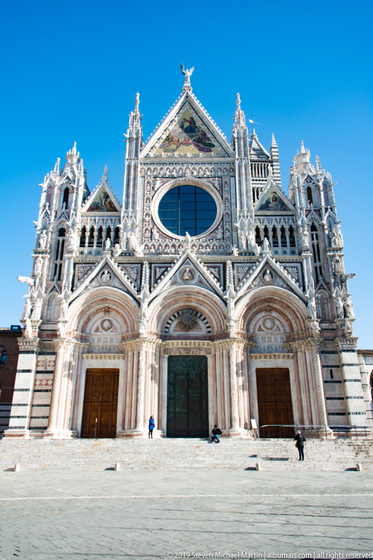 Siena Cathedral’s striped marble west façade with three portals, pointed gables, and an oval window.